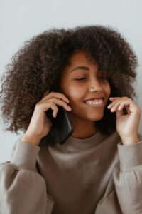 Smiling woman with afro hair enjoying a phone call indoors, wearing a casual sweater.